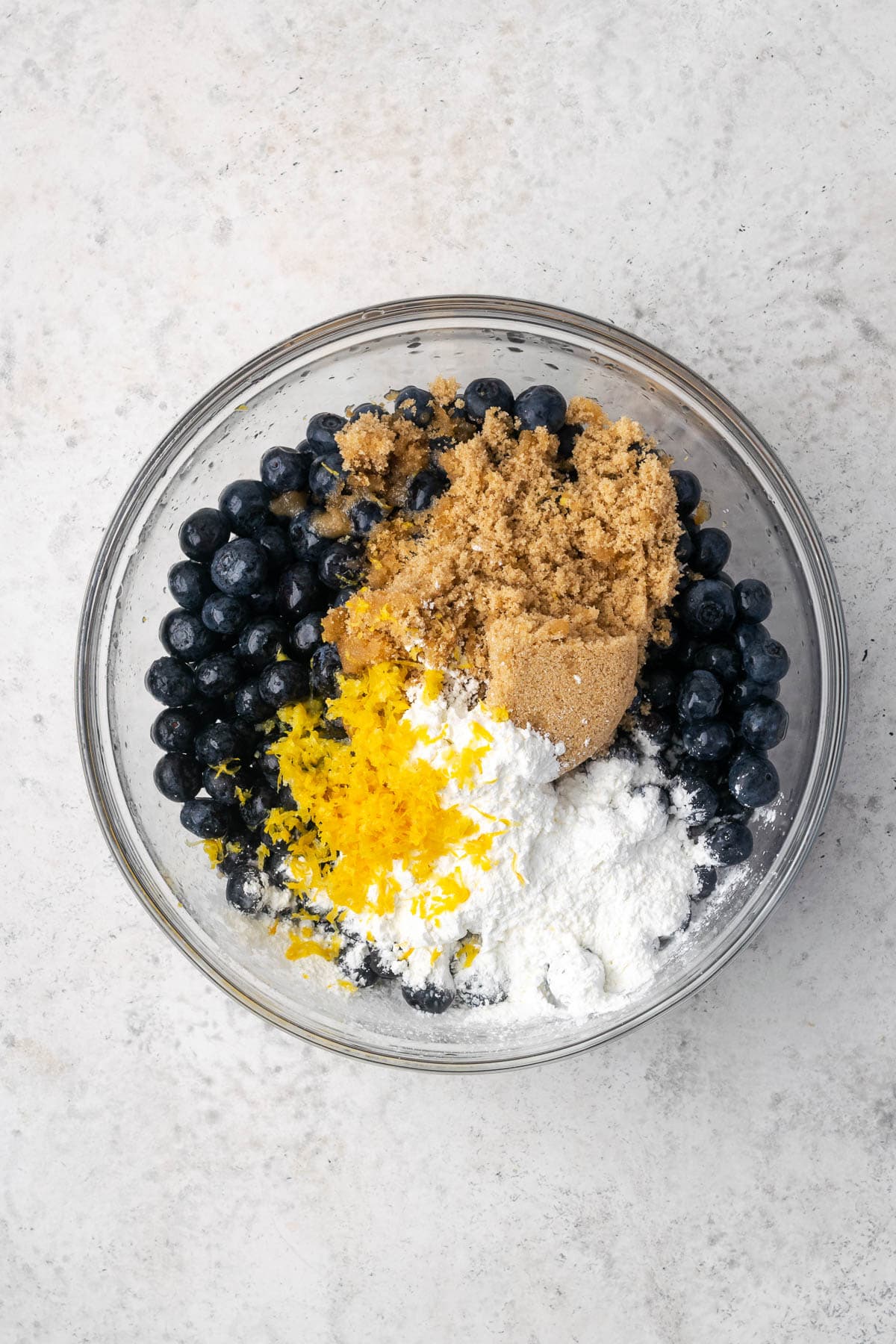 A large mixing bowl filled with blueberries and dry ingredients.