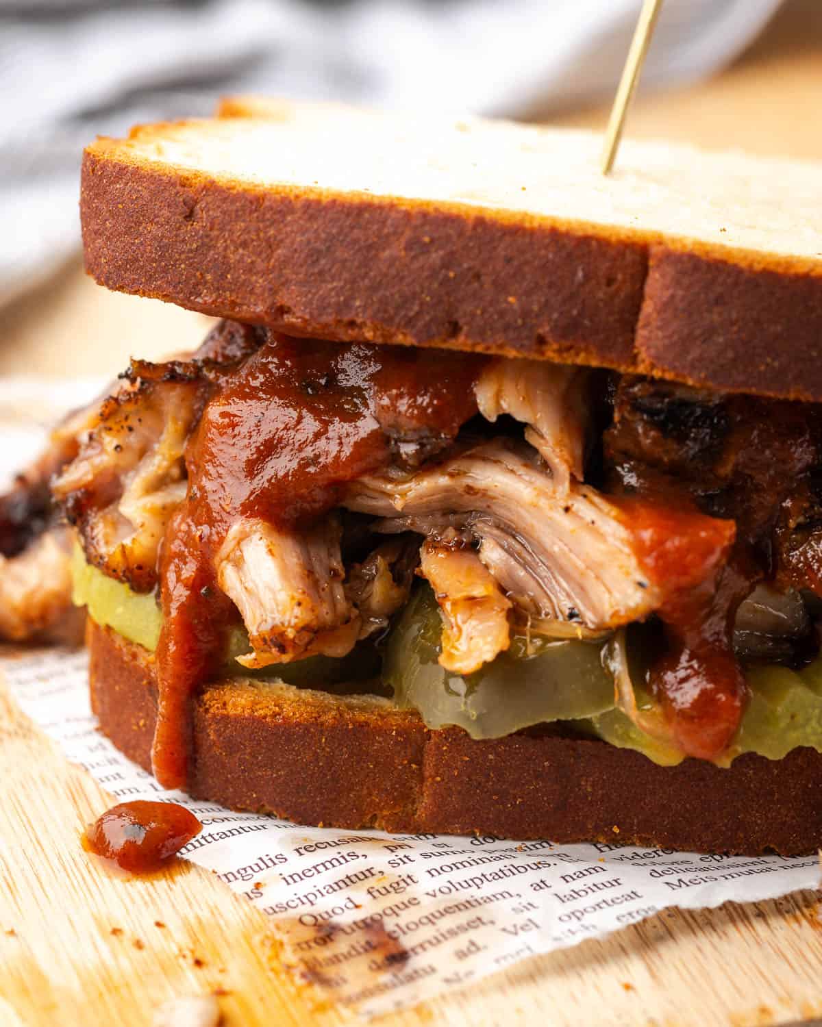 A pulled pork sandwich on gluten free bread served with pickles and bbq sauce.