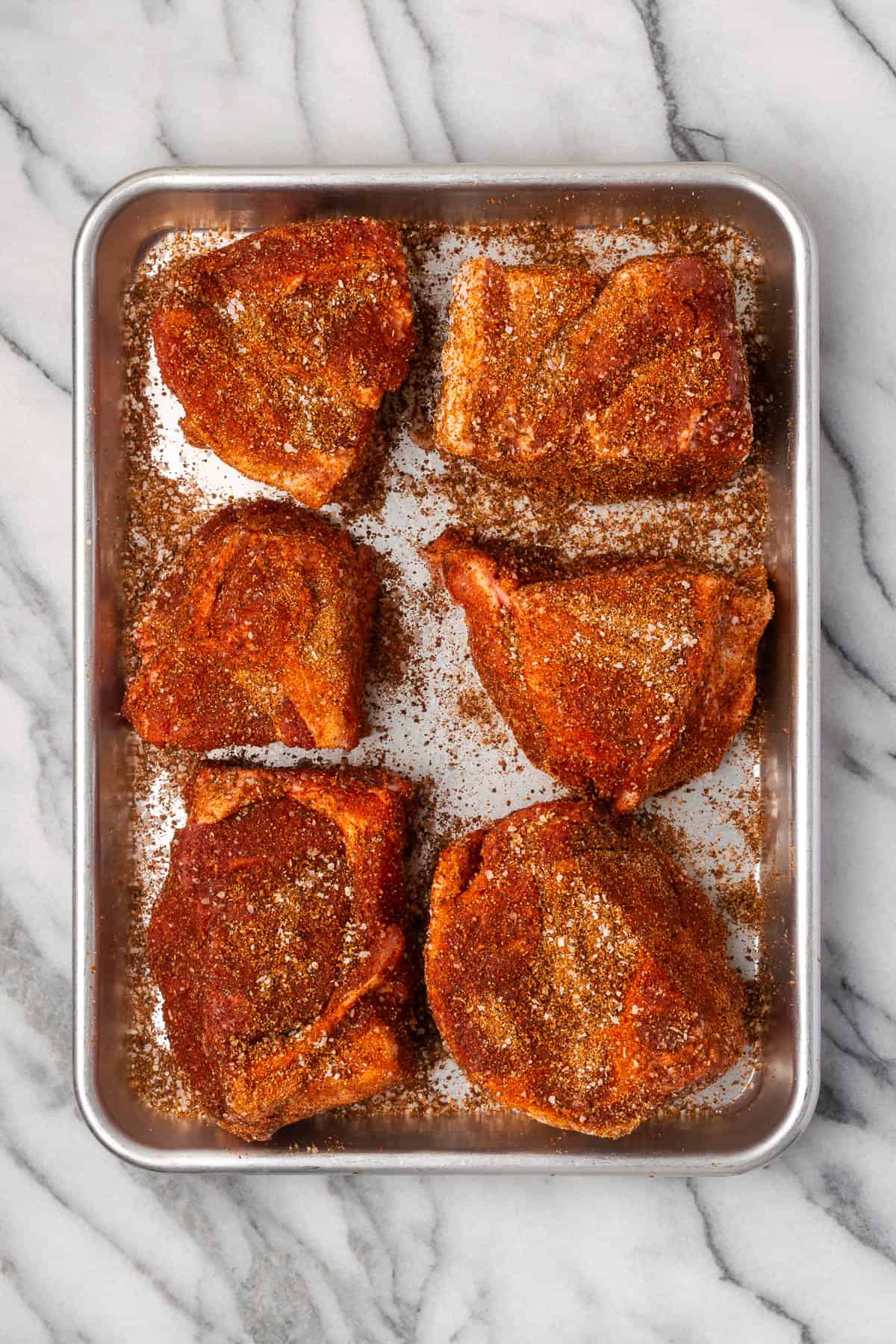 Pork pieces coated with spice rub sitting on a metal baking tray.