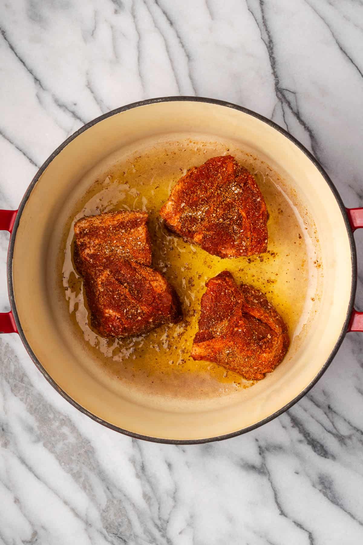 Seasoned pork pieces being seared in a Dutch oven pot.