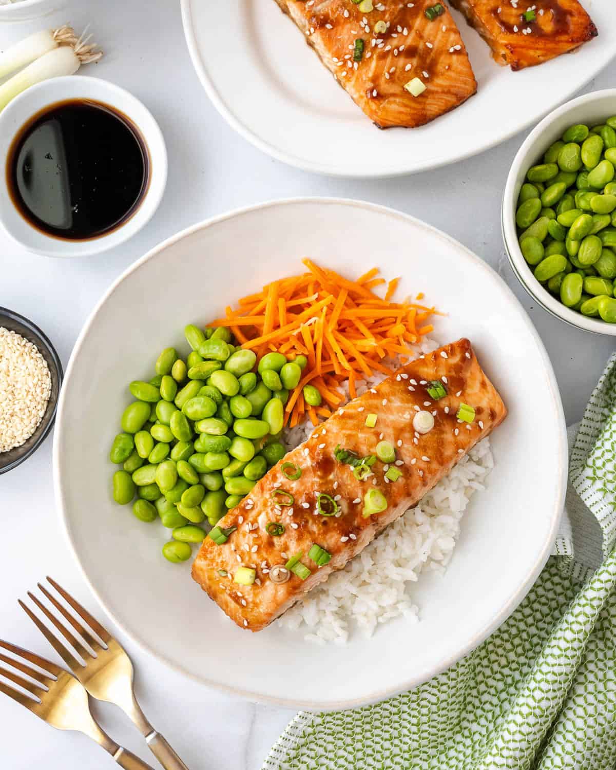 Teryaki salmon served over a bowl of rice, edamame and carrots.