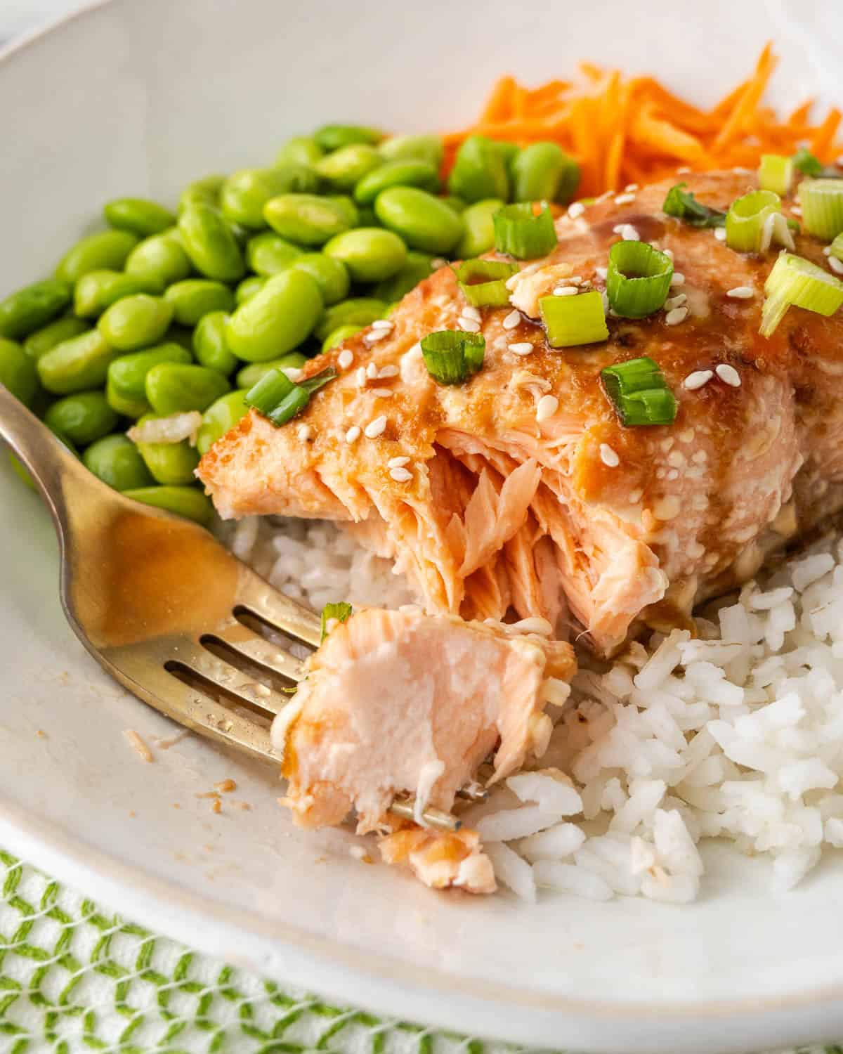 A fork with a bite of teriyaki salmon on a plate of rice.