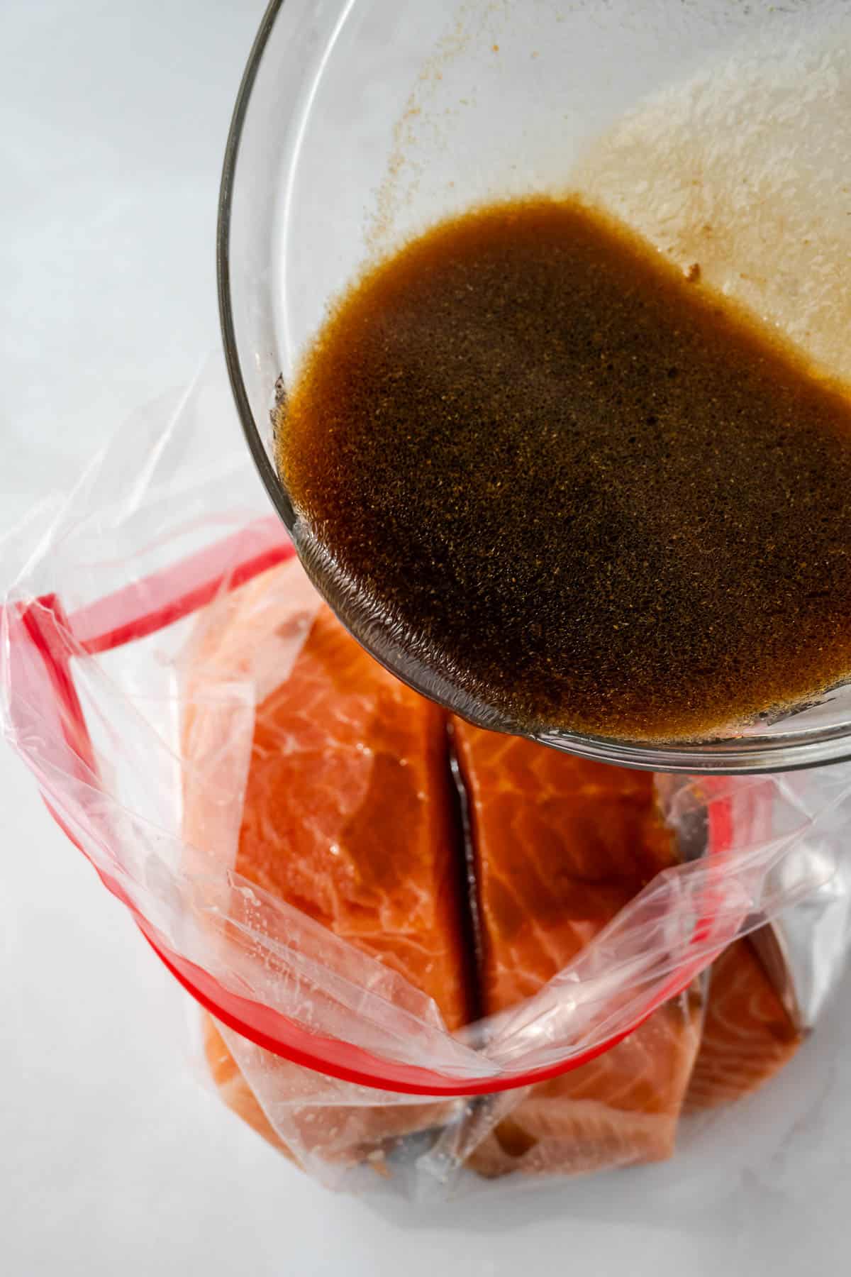 Teriyaki sauce being poured over salmon in a large ziploc bag.
