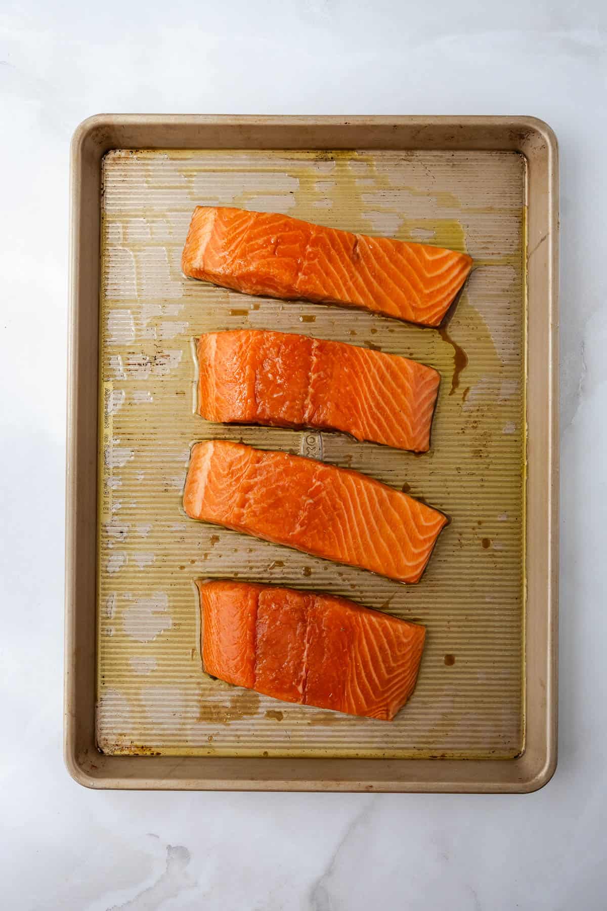 Four salmon filets marinated with teriyaki sauce on a baking sheet.