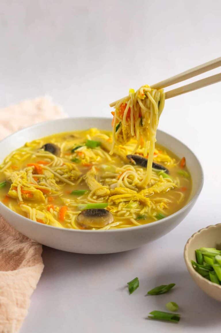 Chopsticks picking up a bite of gluten free ramen from a serving bowl. 