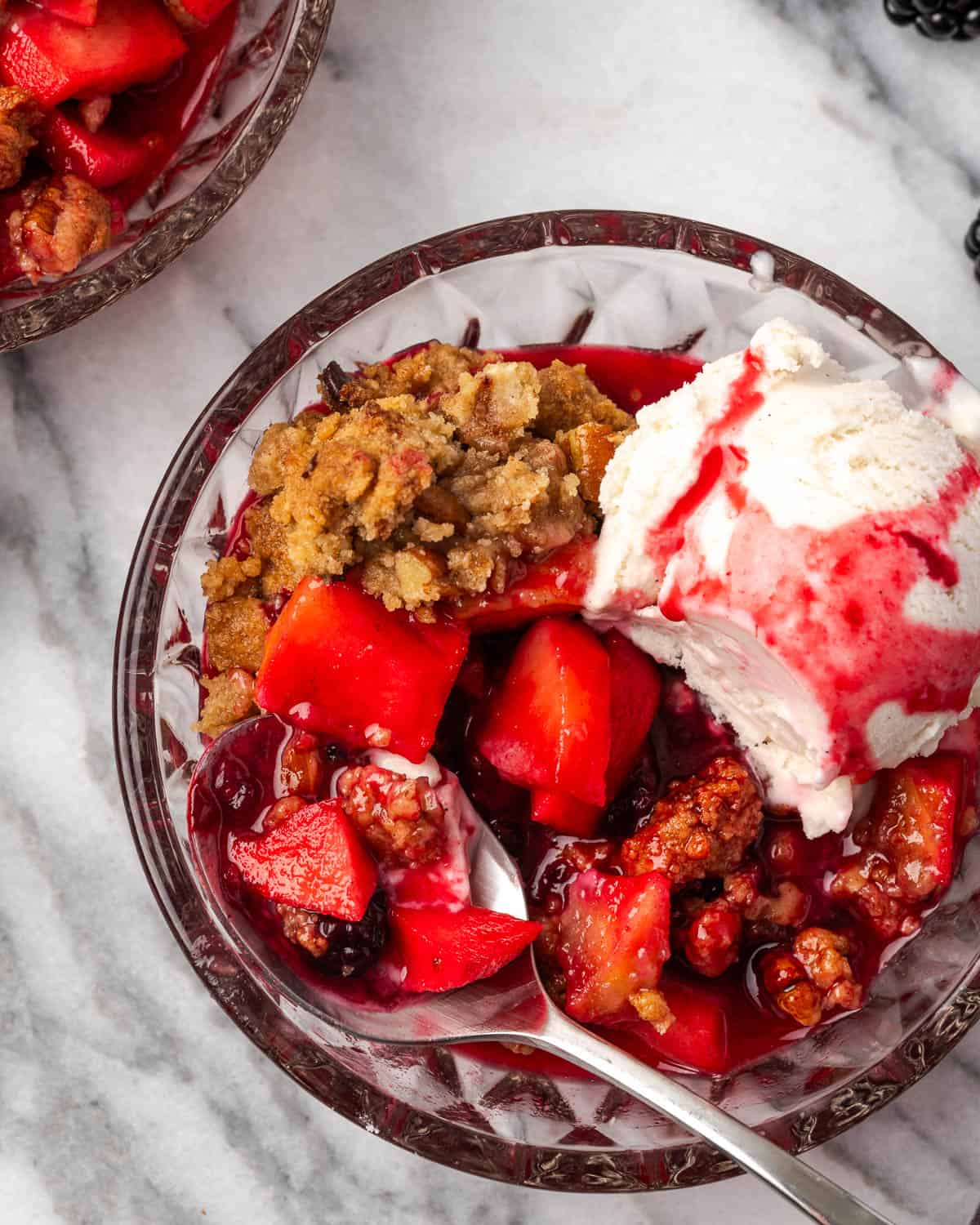A spoon scooping up a bite of apple blackberry crumble with vanilla ice cream.