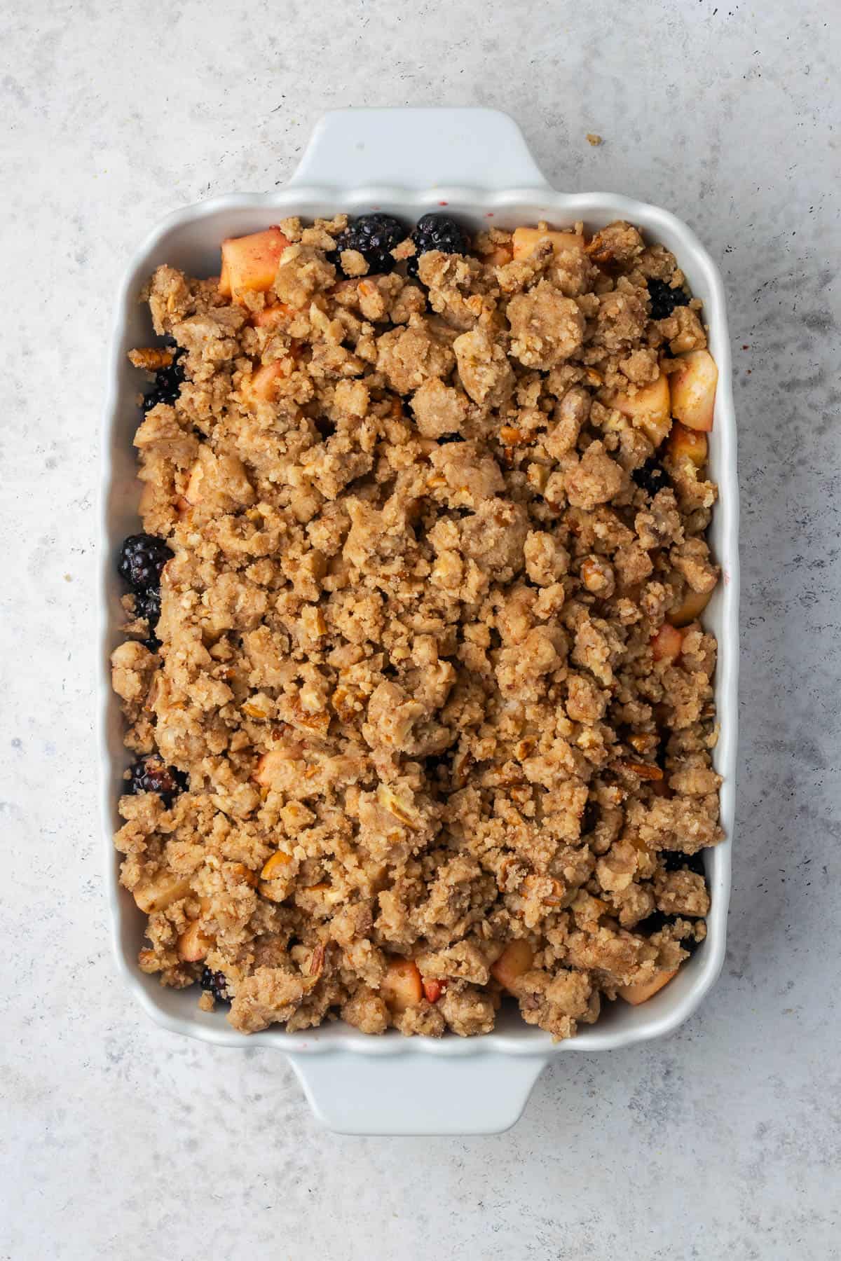 An unbaked apple and blackberry crumble sitting on a white counter.
