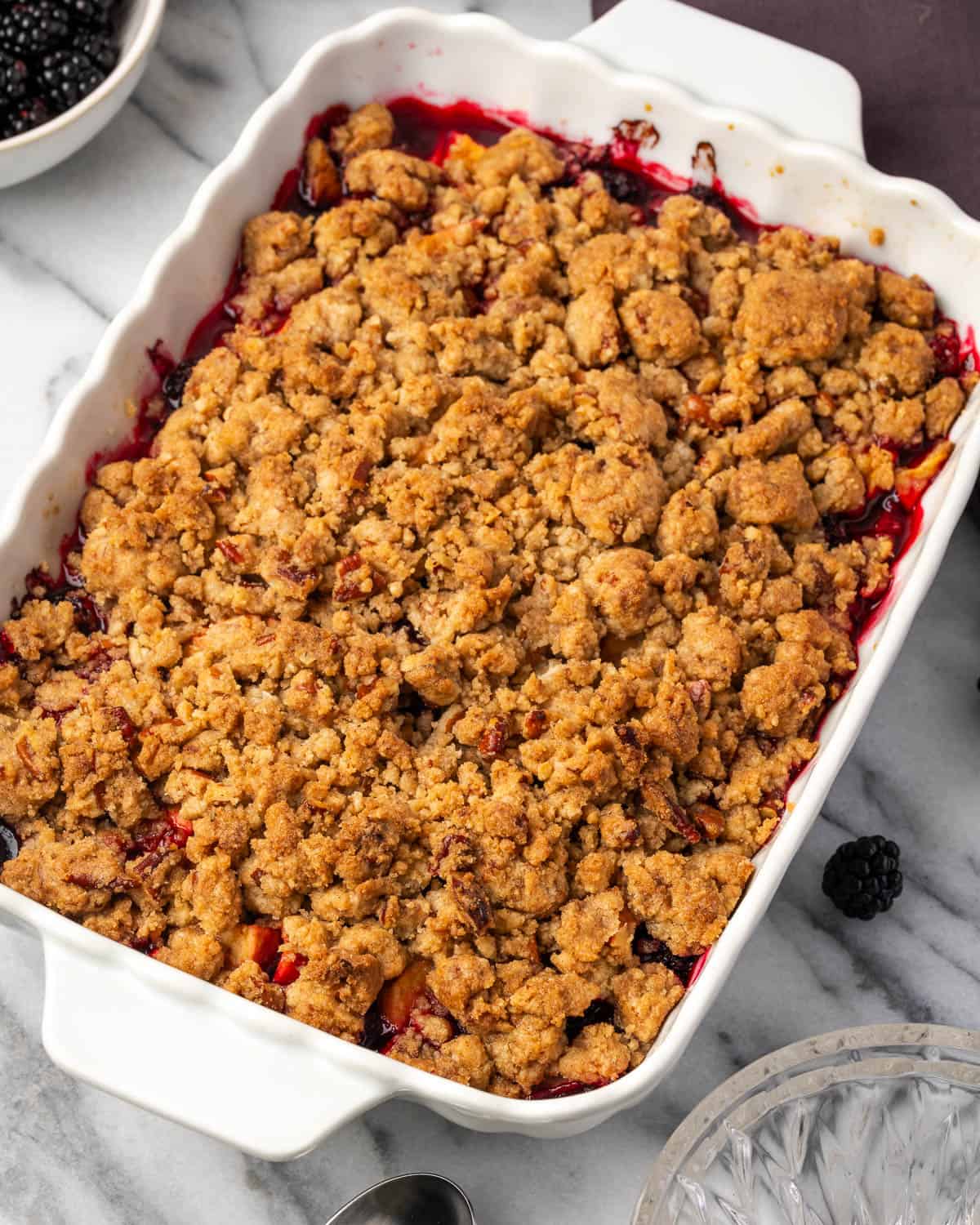 A freshly baked apple and blackberry crumble sitting on a marble counter.