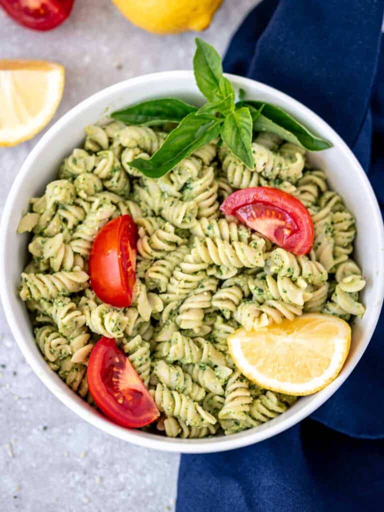 A bowl of pesto pasta served with fresh tomatoes and lemon. 