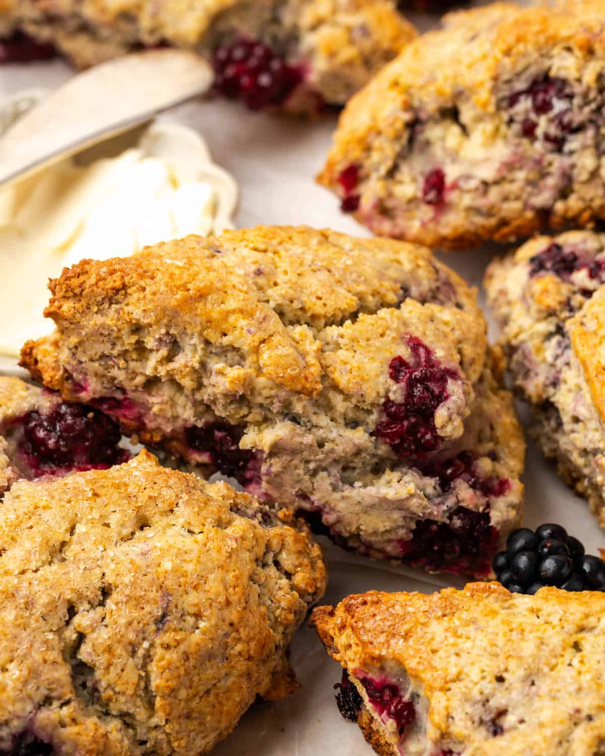 A batch of blackberry scones sitting on a serving tray next to a dish of butter.