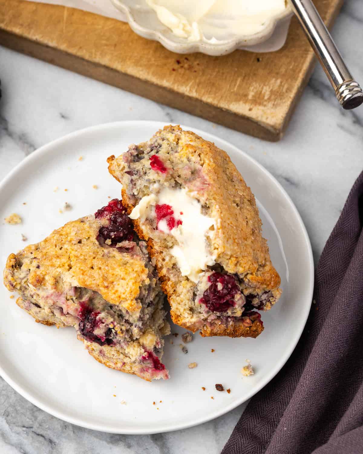 A blackberry scone broken in half and covered with butter sitting on a small serving plate.