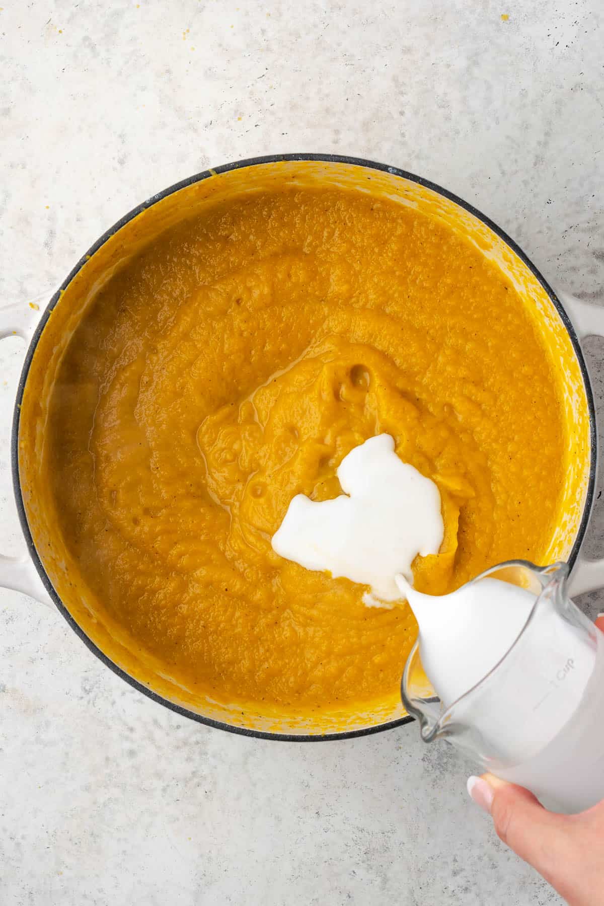 Coconut milk being poured into pureed squash soup.