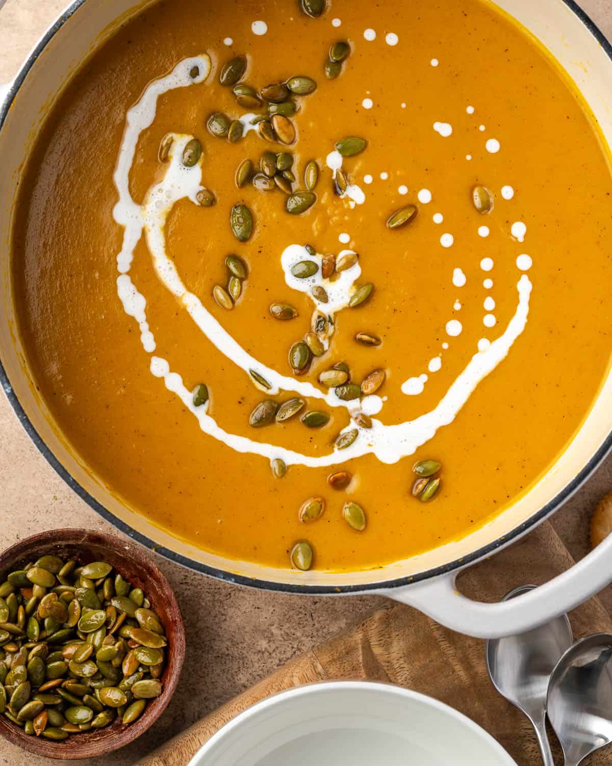 A large pot filled with butternut squash and apple soup garnished with cream and roasted pepitas.