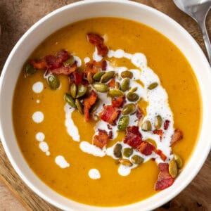 A bowl of butternut squash and apple soup topped with bacon and pumpkin seeds.