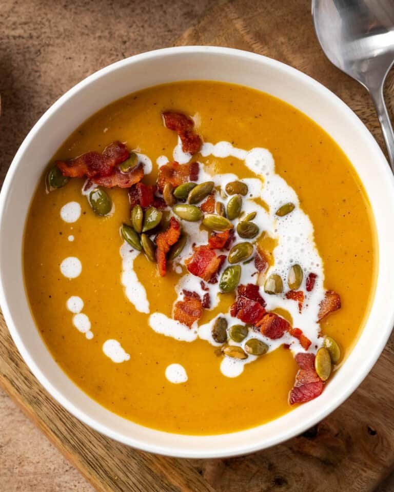 A bowl of butternut squash and apple soup topped with bacon and pumpkin seeds.