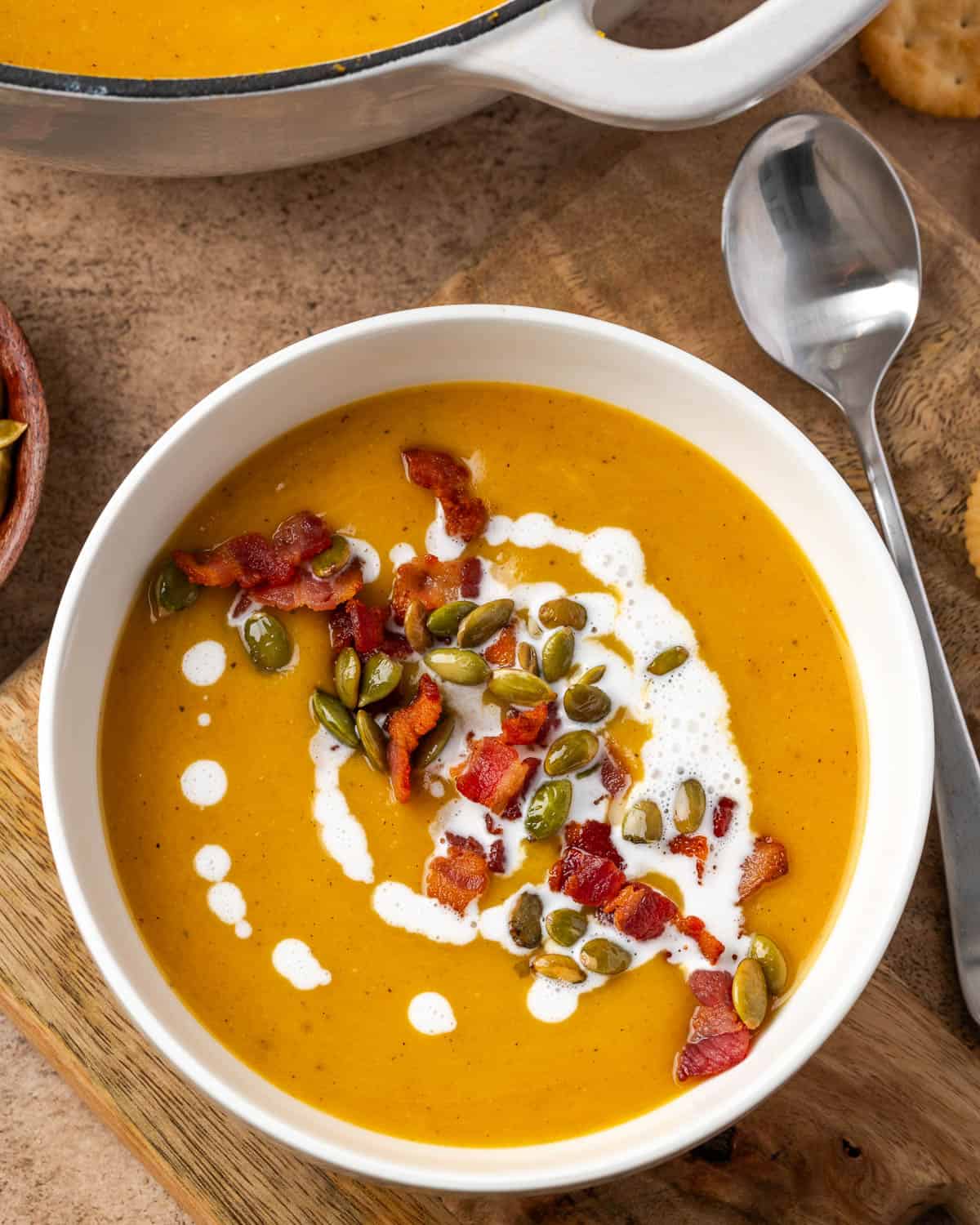 A bowl of butternut squash and apple soup topped with bacon pieces and roasted pumpkin seeds.