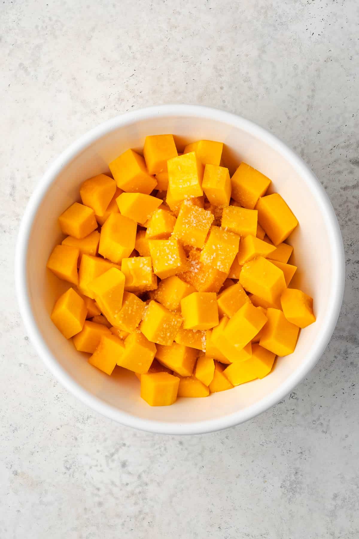 Butternut squash cubes, olive oil, maple syrup and salt combined in a large bowl.