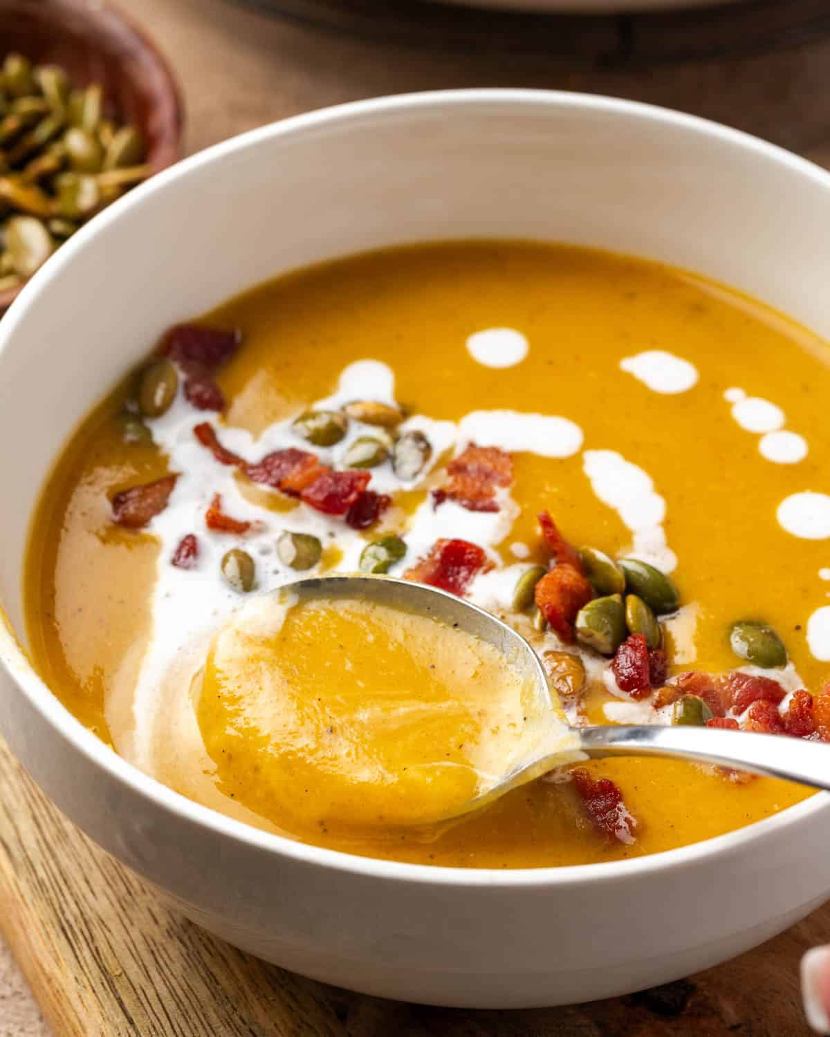 A spoon scooping a bite of creamy butternut squash soup from a serving bowl.