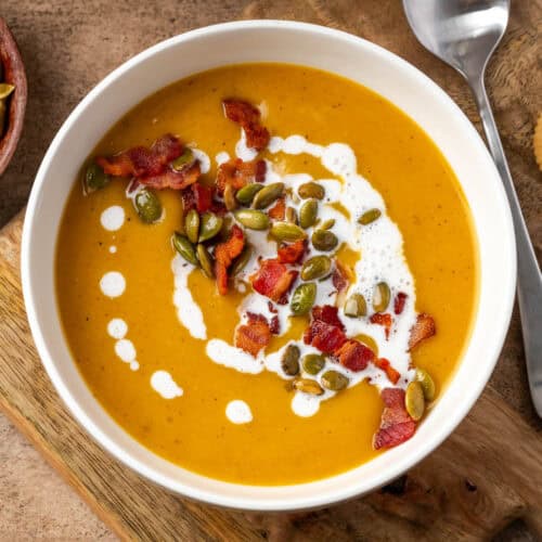 A bowl of butternut squash and apple soup topped with bacon and pumpkin seeds.