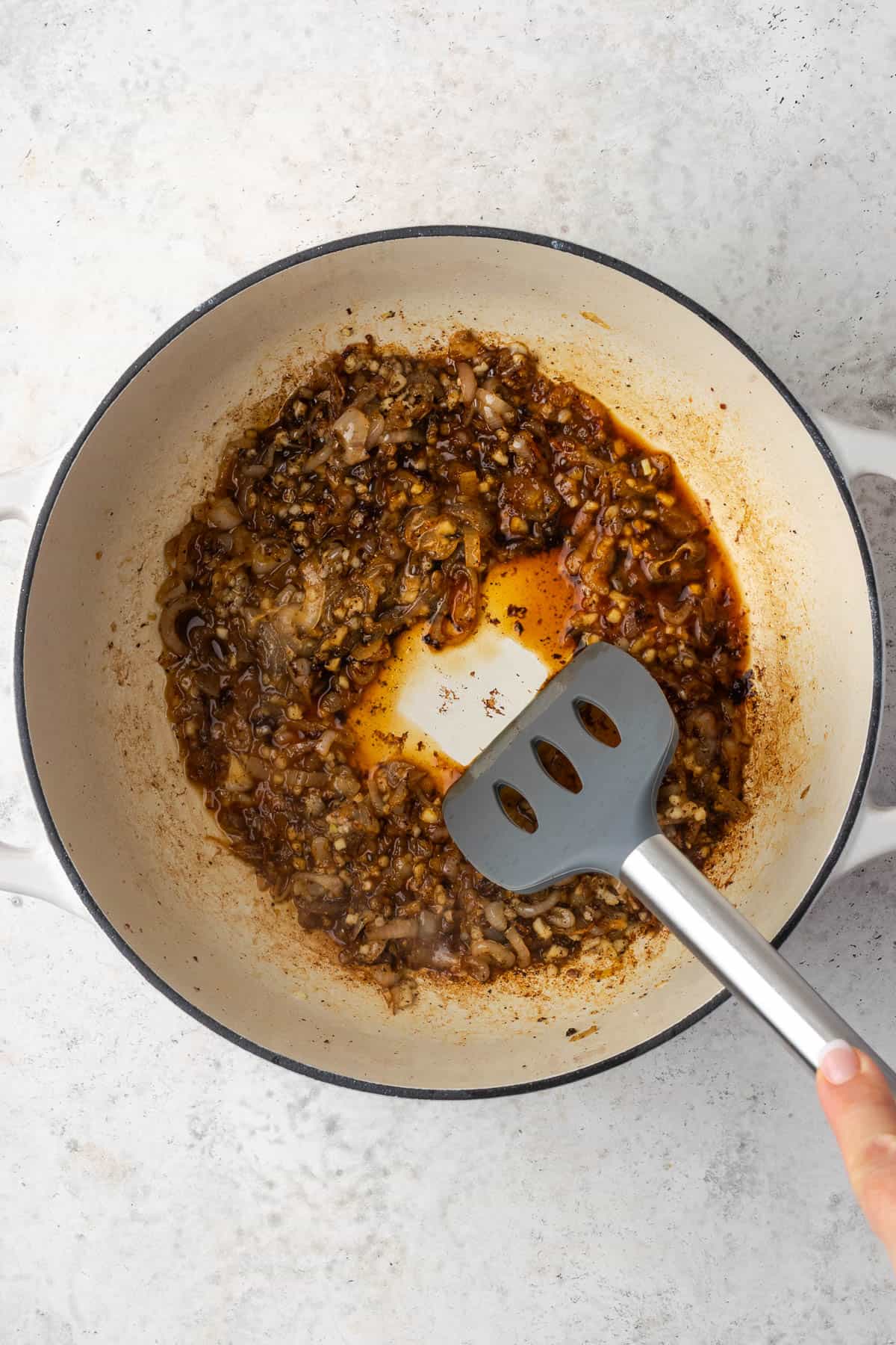 A spatula scraping the cooked bits from the bottom of the pot.