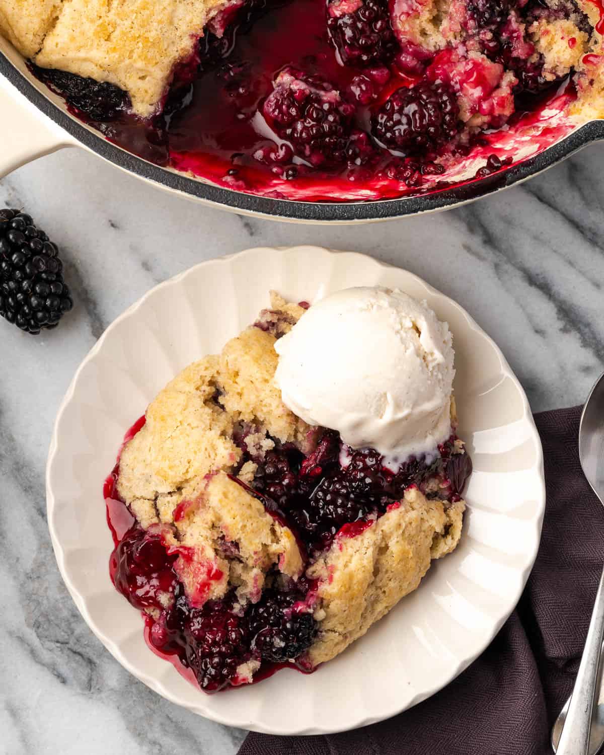 A plate of gluten free blackberry cobbler served with a scoop of vanilla ice cream. 