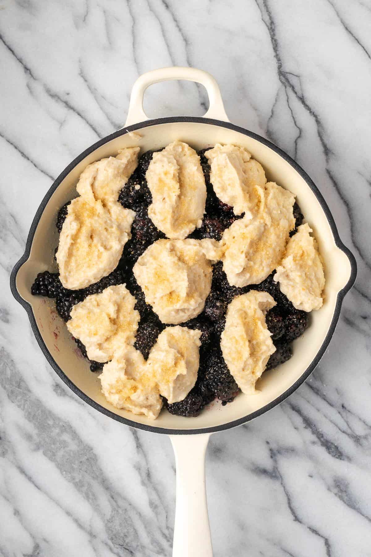 A unbaked blackberry cobbler sitting on a marble counter.