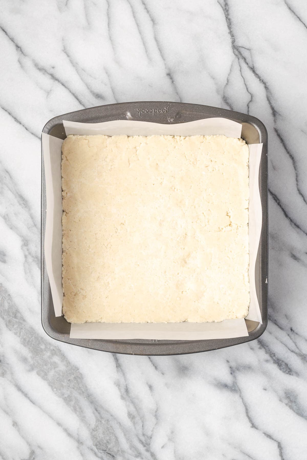 An unbaked shortbread crust in a small square pan.