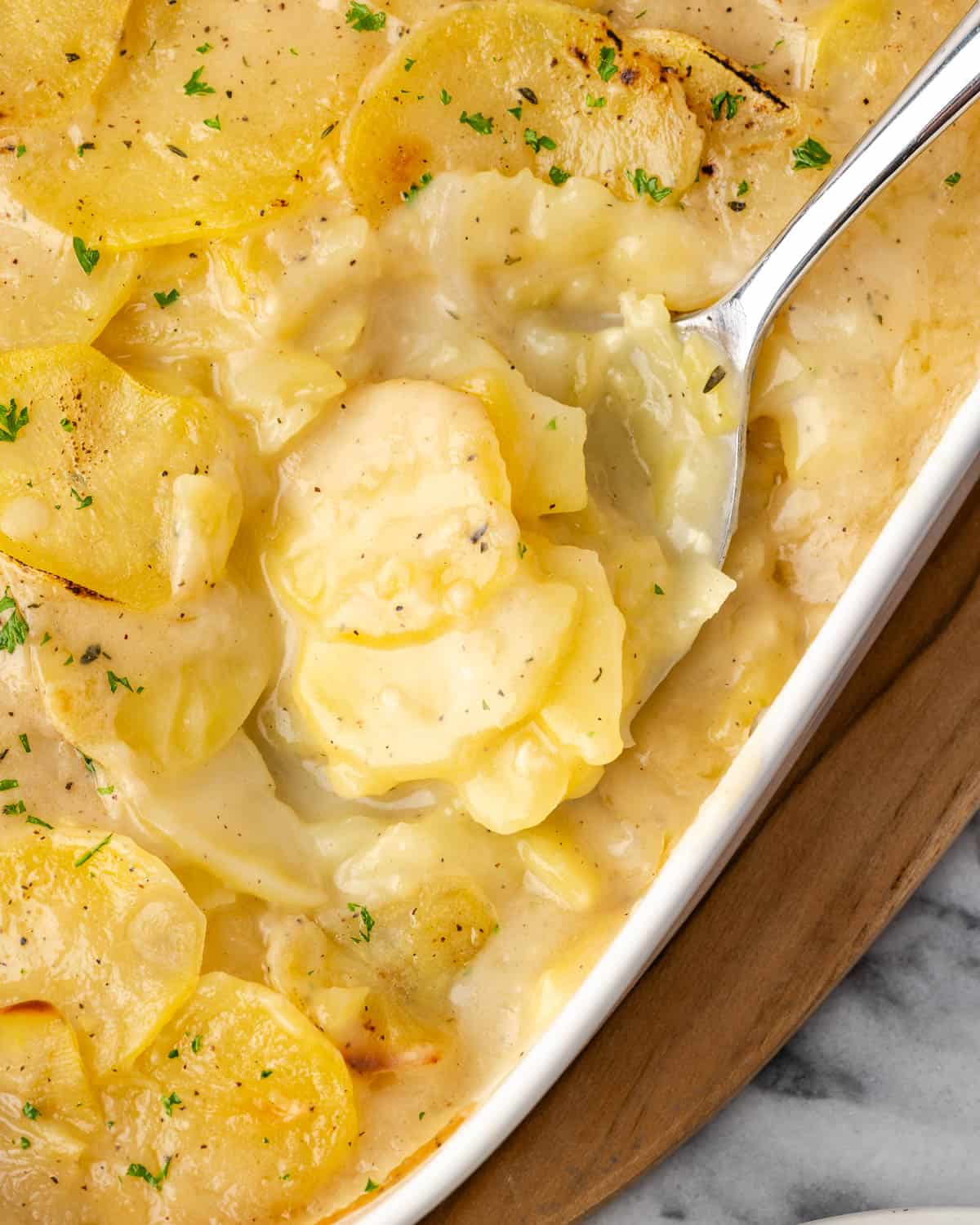 A serving spoon scooping scalloped potatoes from a casserole dish.
