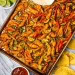 Chicken fajitas on a large sheet pan served with chips and salsa.