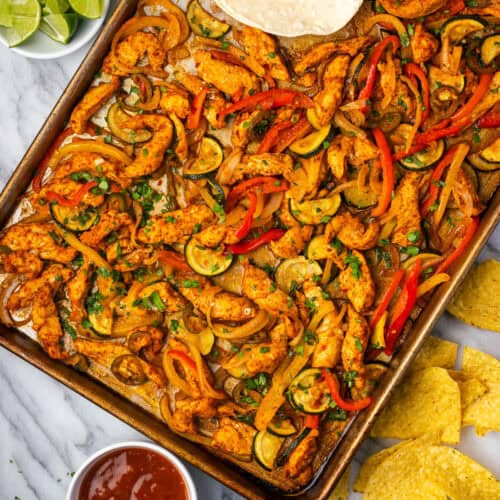 Chicken fajitas on a large sheet pan served with chips and salsa.