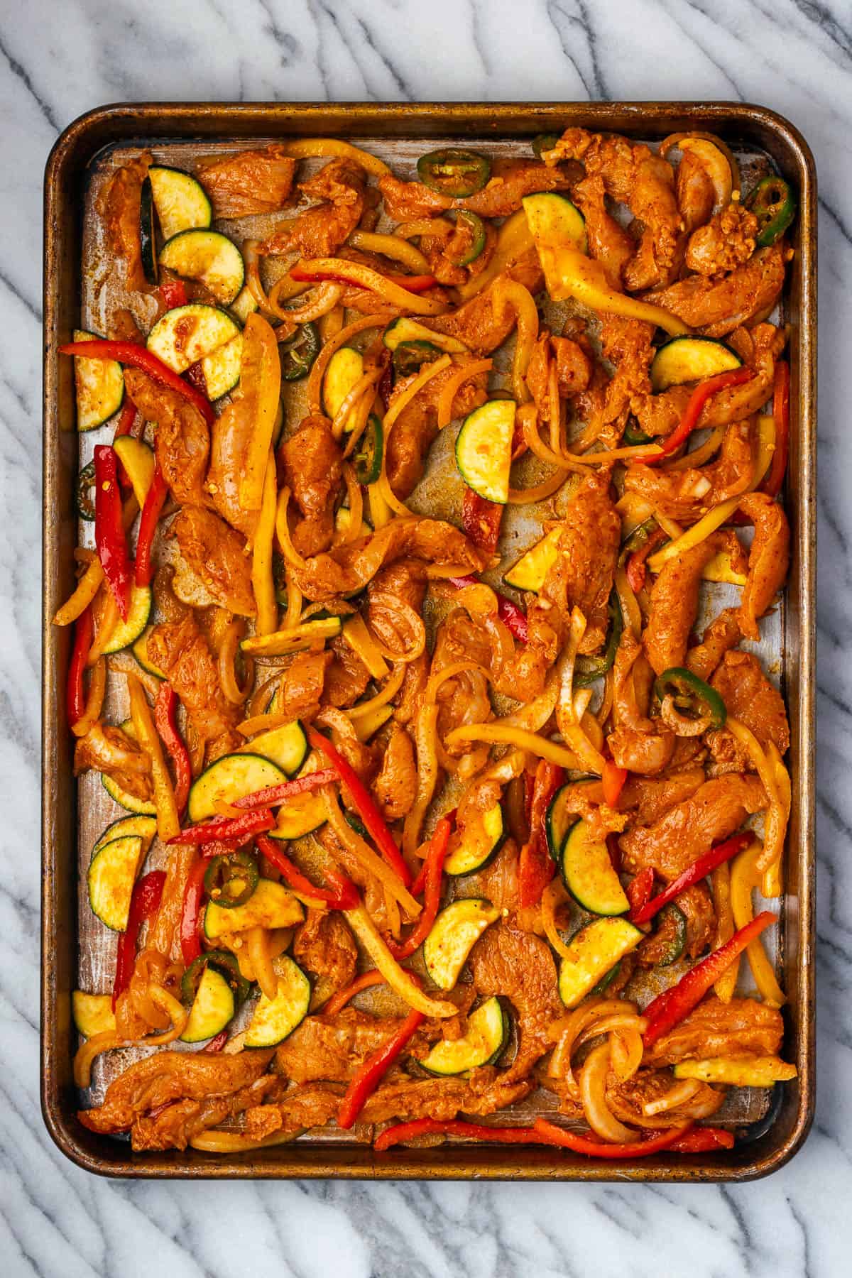 Uncooked chicken fajitas spread on a large sheet pan. 