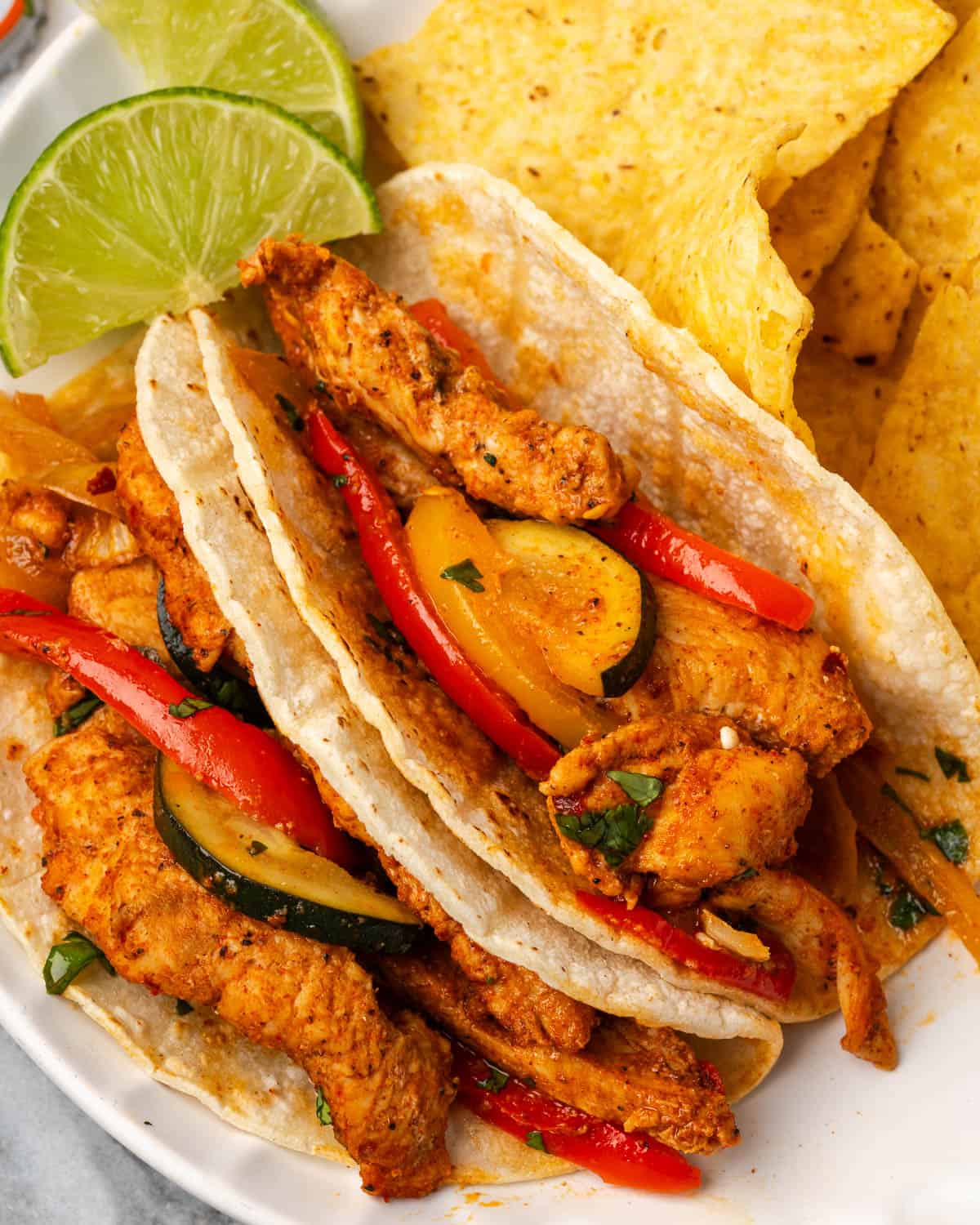 Two corn tortillas filled with chicken fajitas served on a plate with corn chips. 