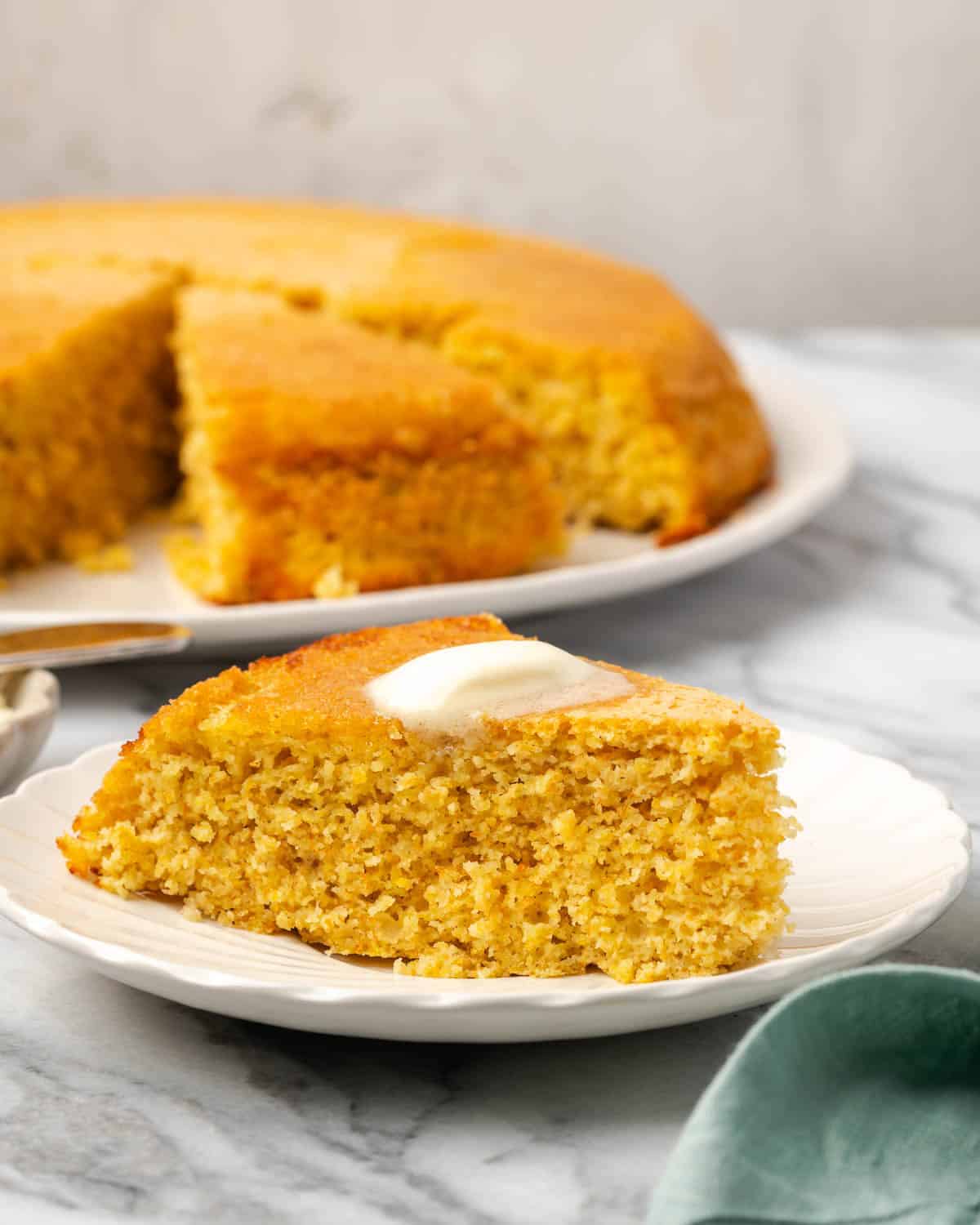 A slice of cornbread topped with butter served on a small plate.