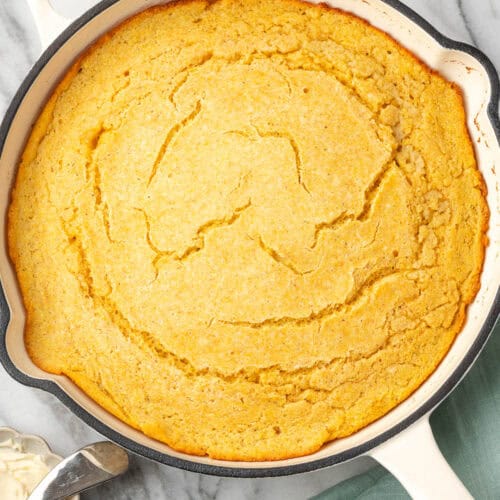 Southern style cornbread baked in a cast iron skillet sitting on a marble counter.
