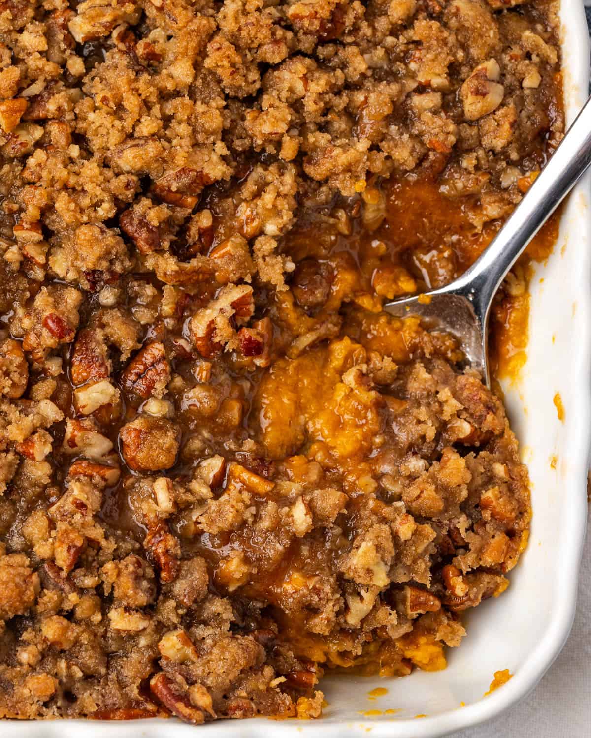 A serving spoon scooping into a sweet potato casserole topping with pecan streusel.
