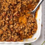 A serving spoon scooping into a pan of sweet potato casserole.