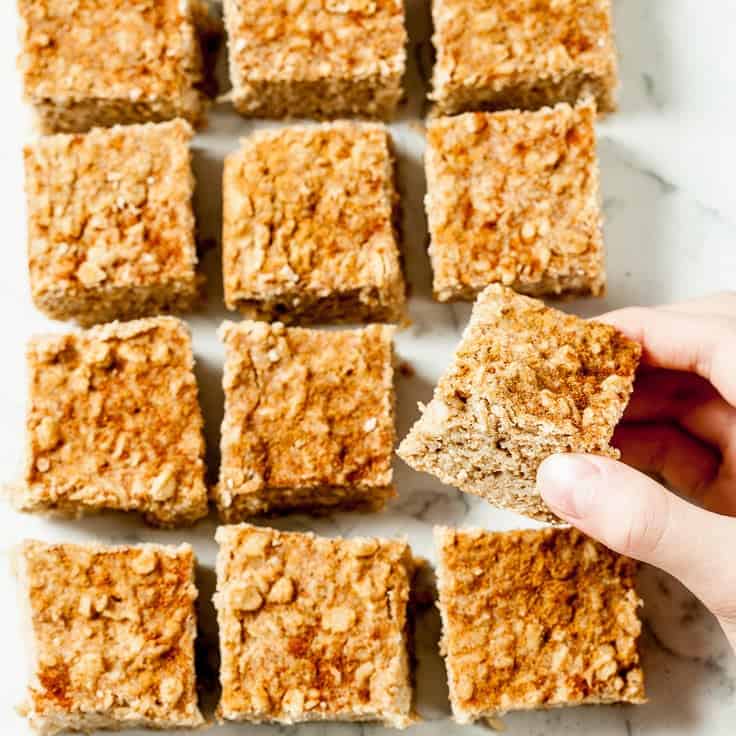 A hand picking up an apple oatmeal bar from the counter.