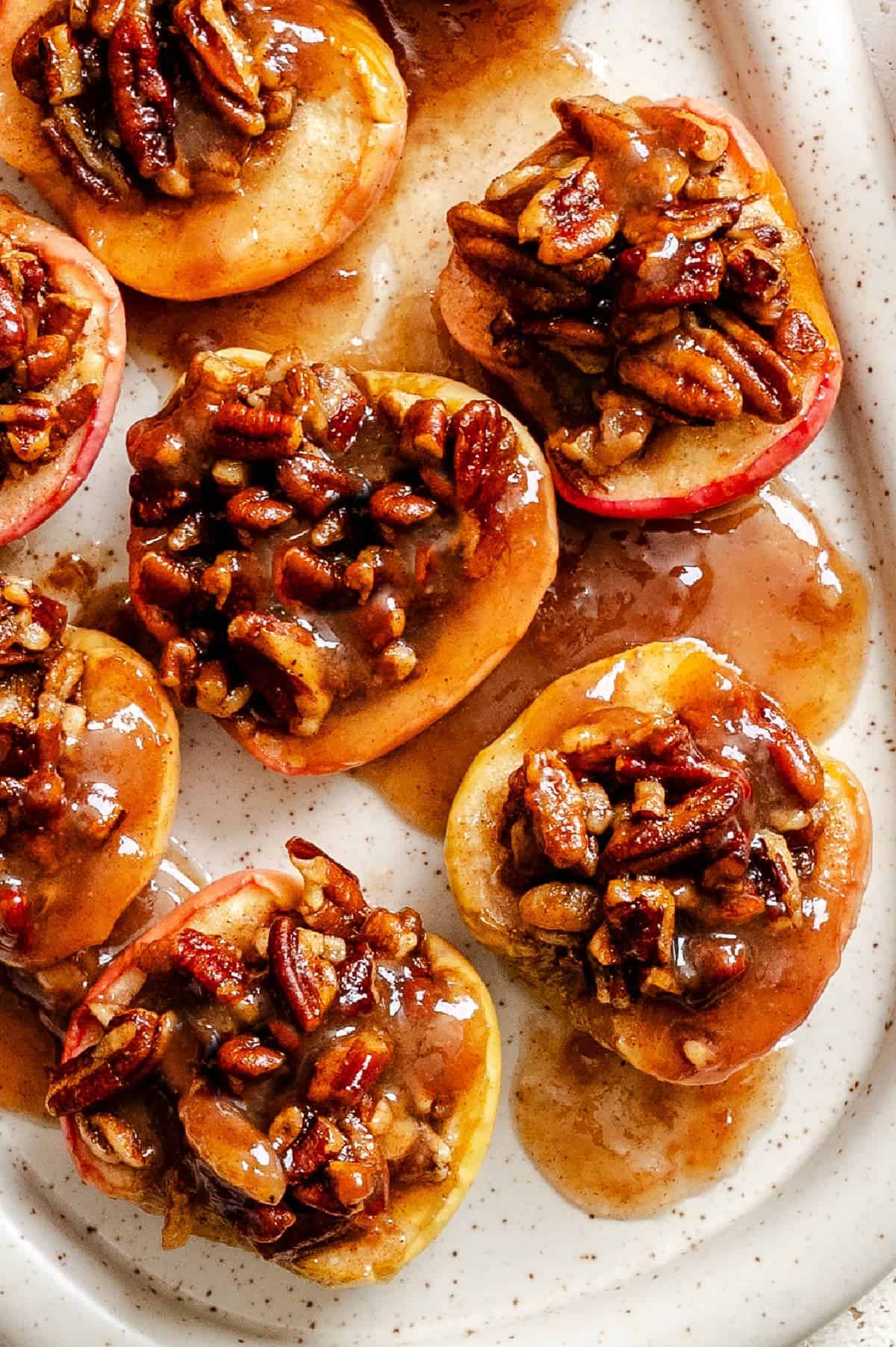 Several baked apples topped with nuts and a golden sauce.