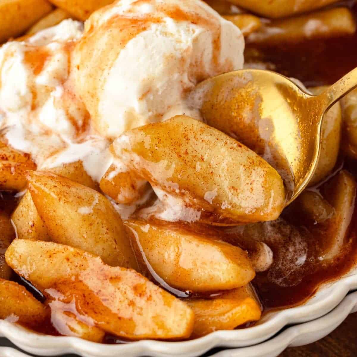 A spoon picking up a bite of fried apples from a serving bowl.