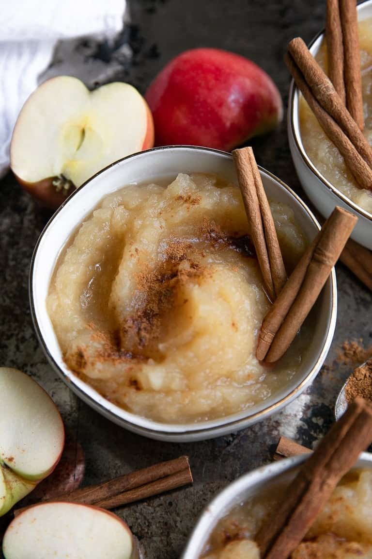 Homemade applesauce in a small bowl topped with ground cinnamon and garnished with cinnamon sticks.