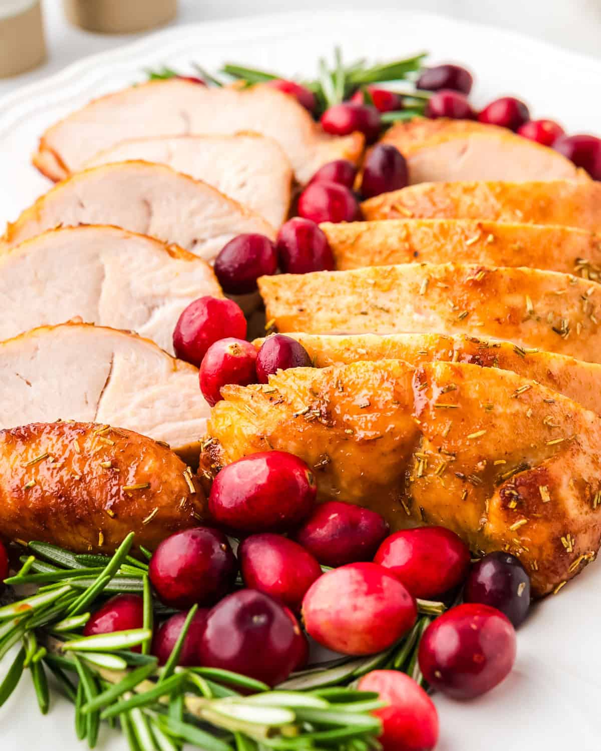 A roasted turkey tenderloin cut into slices on a serving platter garnished with fresh cranberries.