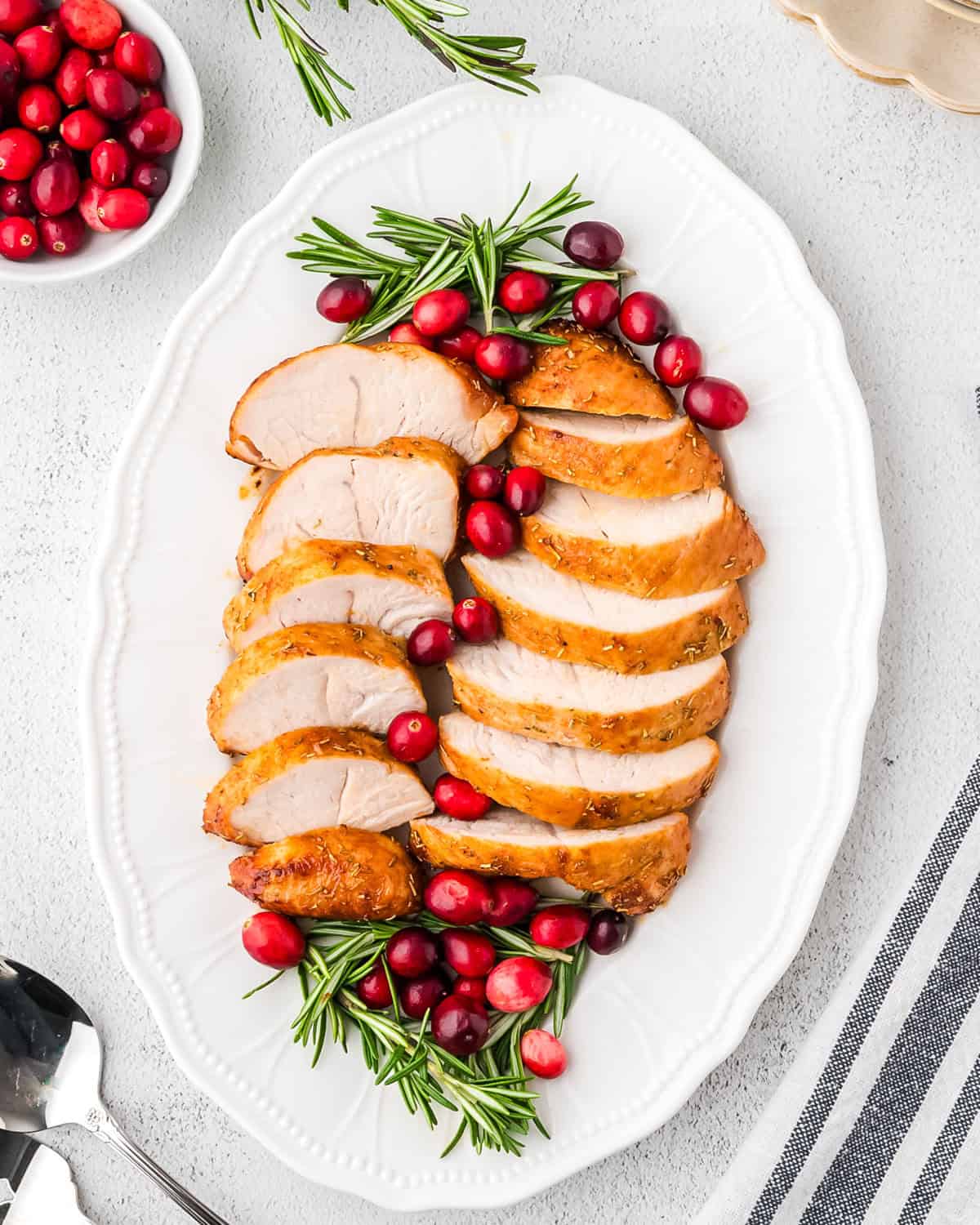 Cooked turkey tenderloin cut into slices on a serving tray garnished with fresh cranberries and rosemary sprigs.