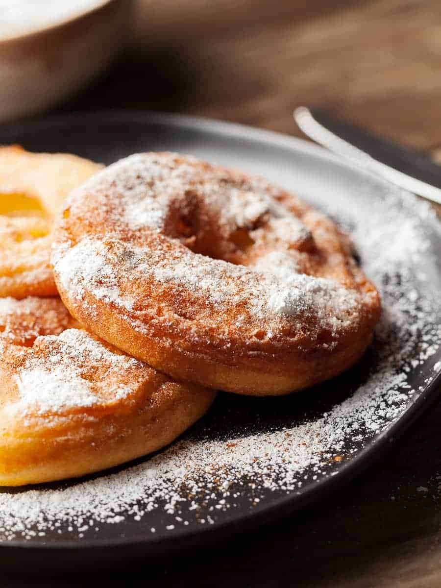 Several fried apple rings topped with powdered sugar sitting on a plate.
