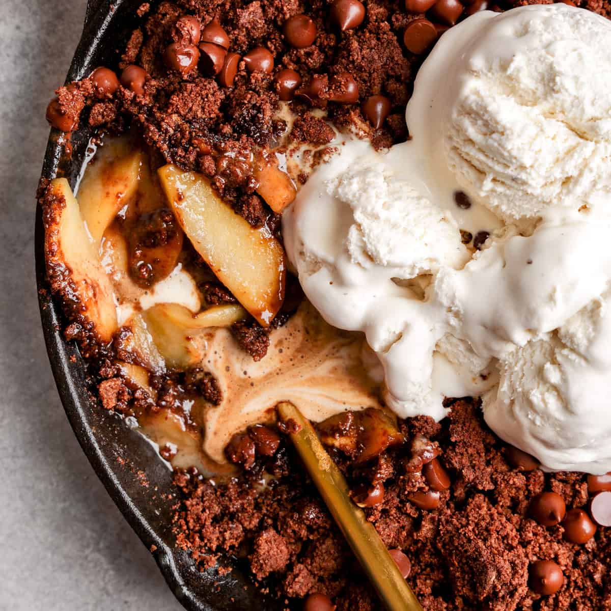 A chocolate apple crisp topped with scoops of vanilla ice cream.