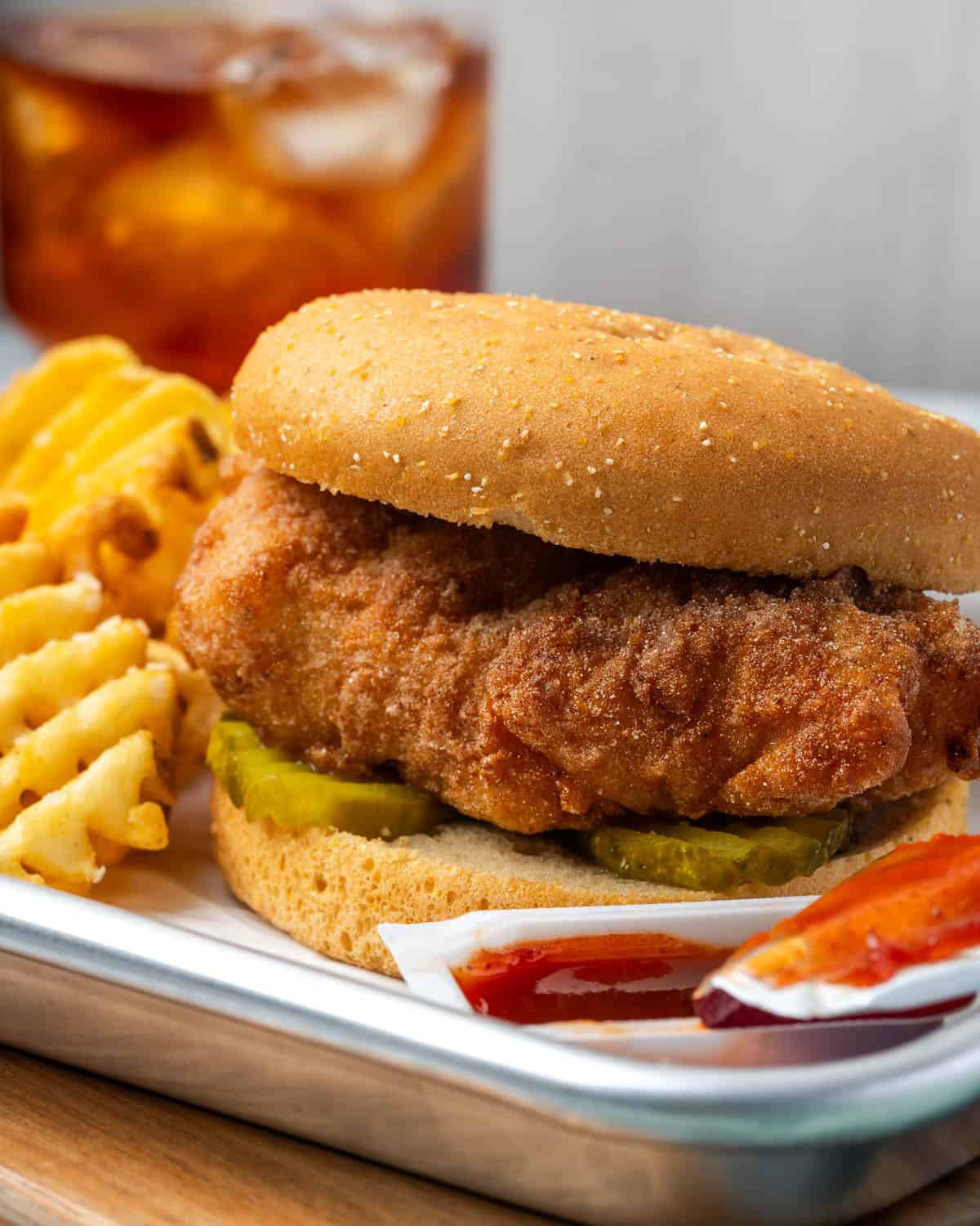 A homemade chick fil a sandwich served with waffle fries and sauce.