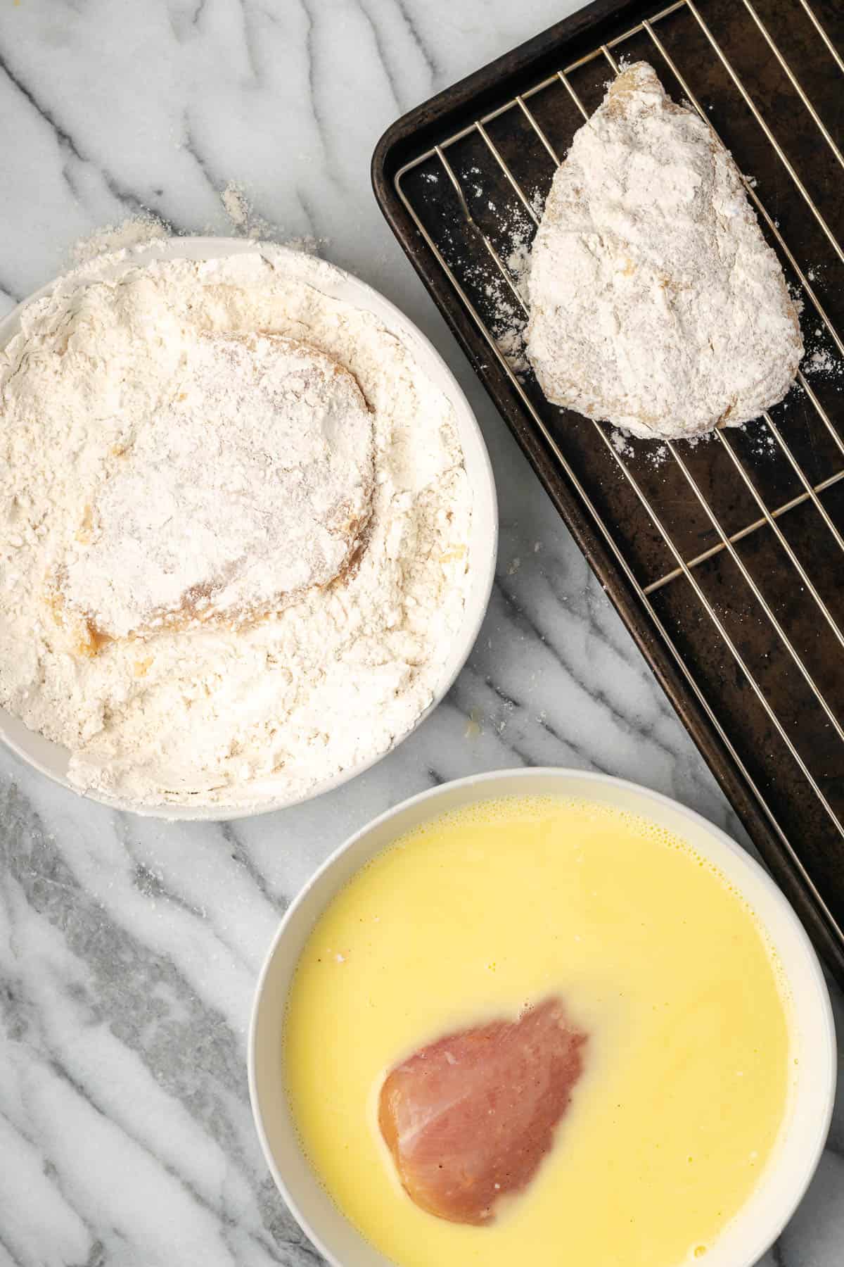 Raw chicken being dredged in egg and flour then placed on a baking sheet.
