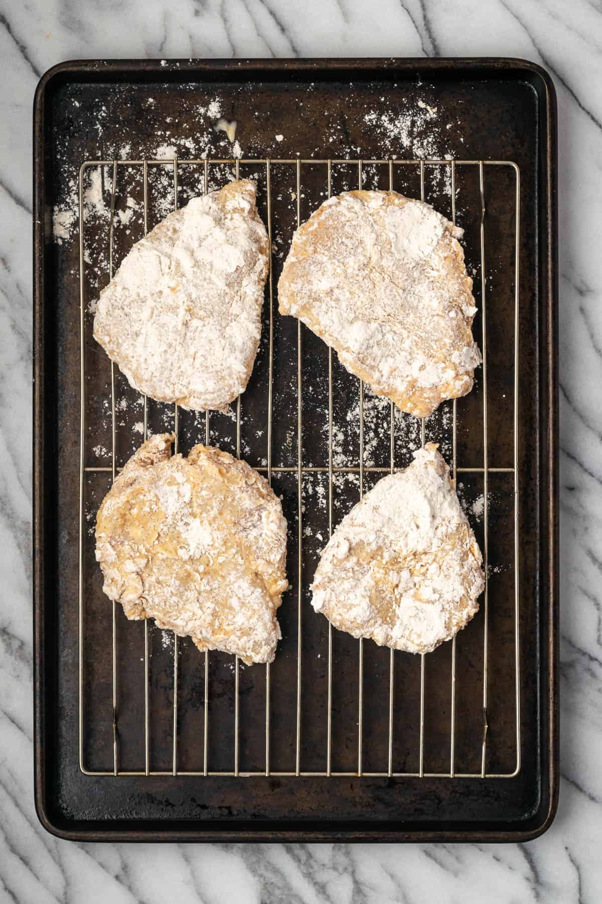Breaded chicken breasts sitting on a wire rack over a baking sheet.