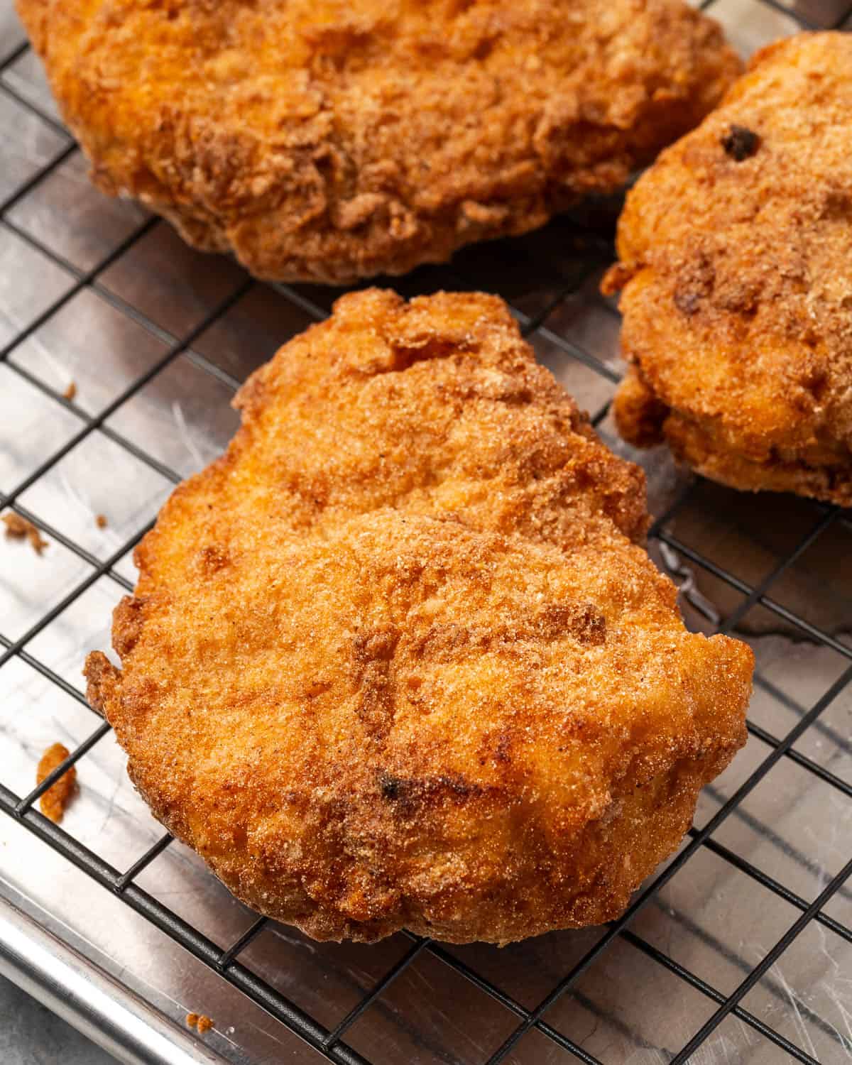 Three fried chicken breasts cooling on a wire rack.