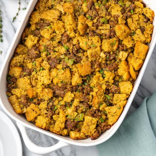 Cornbread stuffing in a white casserole dish sitting on a marble counter.