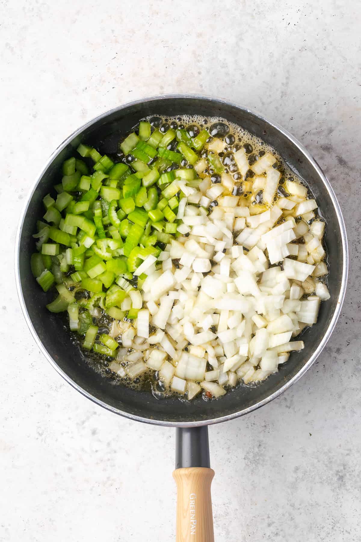 Diced onions and celery being sauteed in a skillet.